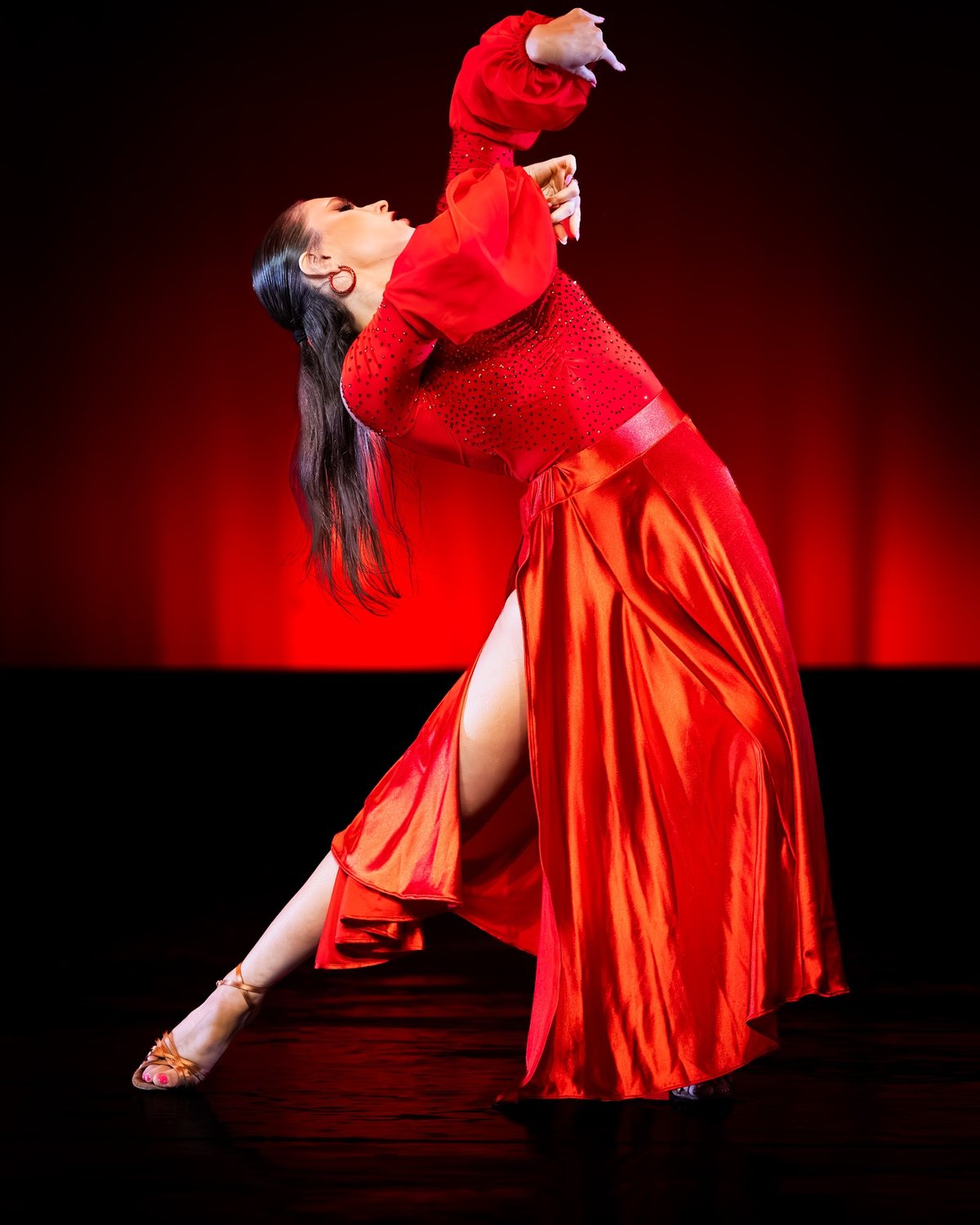 A dancer in a red satin gown with full red sleeves leans back in a long diagonal line on a red-lit stage at Dancing Stars 2026