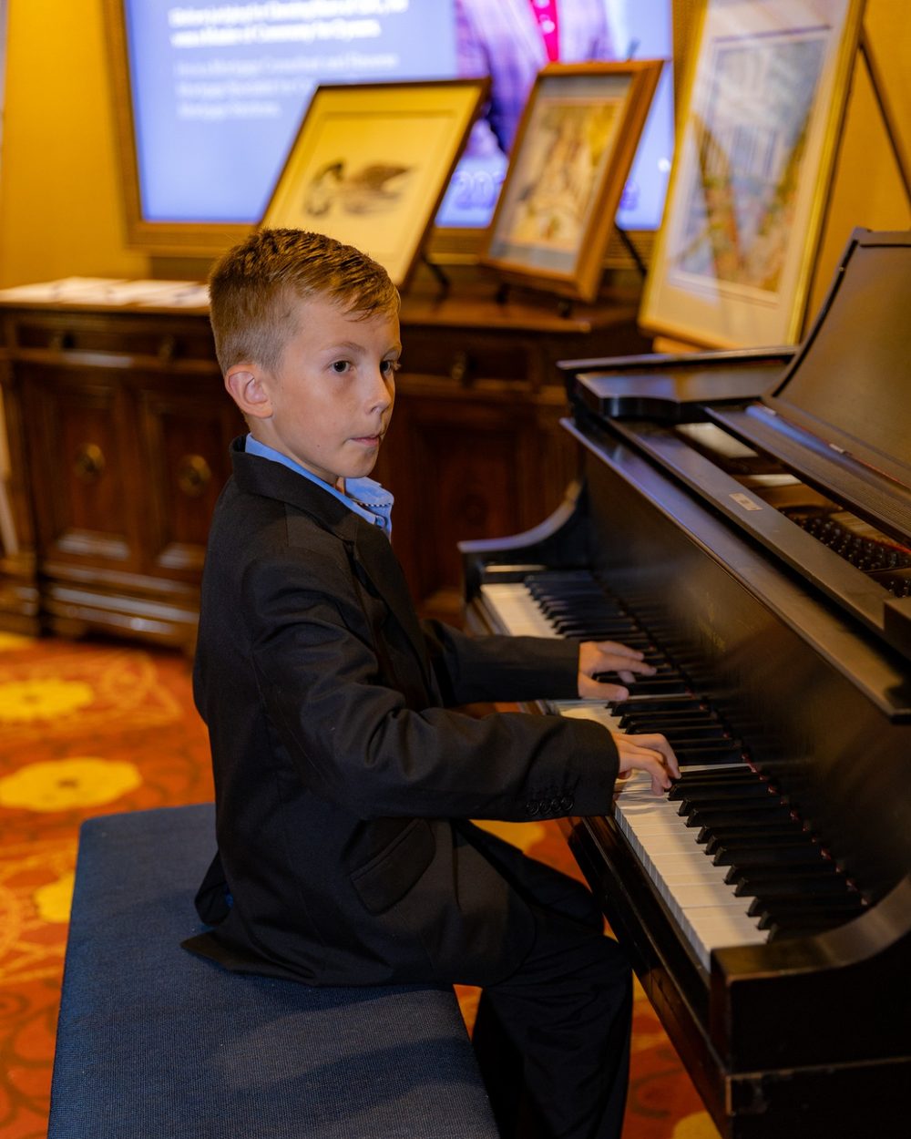 A young boy in a dark suit playing a grand piano at Dancing Stars 2025